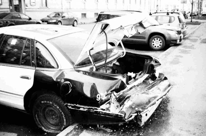 A damaged car missing the back fender and with the trunk open.