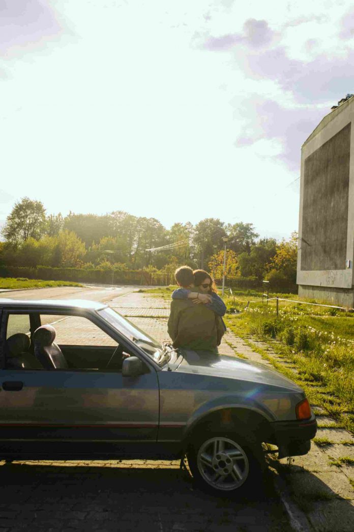 A man and a woman hugging on the hood of a car.