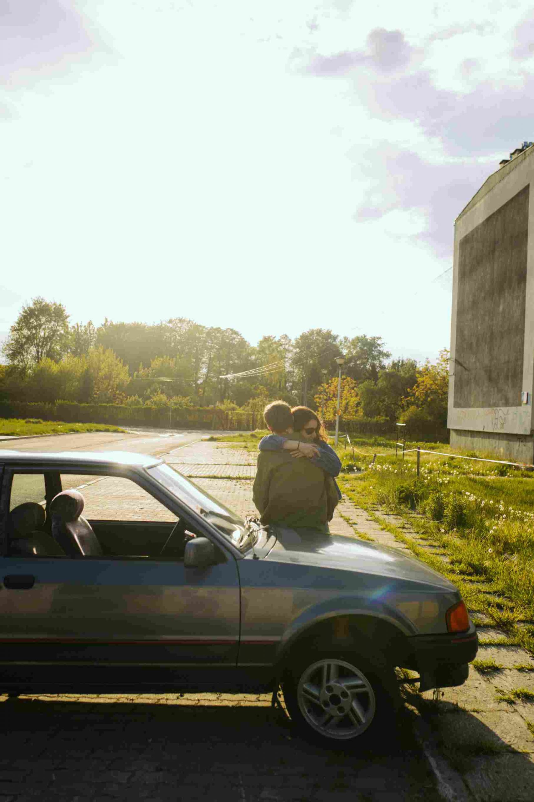 A man and a woman hugging on the hood of a car.